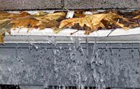 A gutter with leaves in it and water coming out of the bottom.
